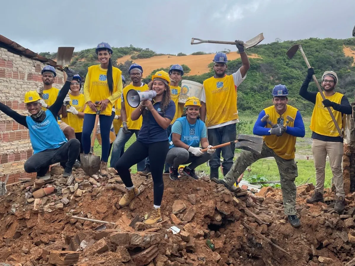 Voluntários da ReforAMAR de capacete, com pás e marretas, comemorando no meio de uma obra