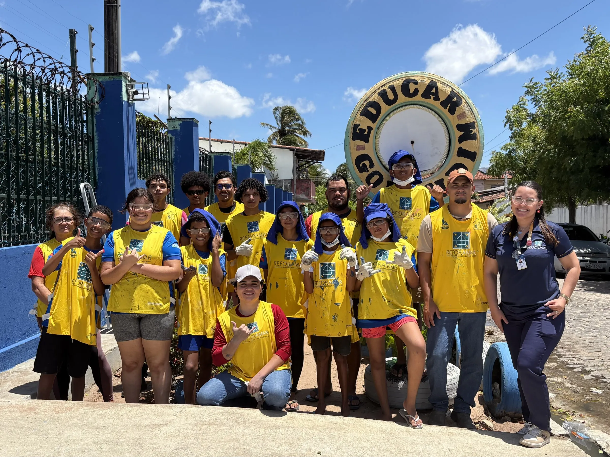 Jovens do projeto Juventude Solidária com coletes amarelos da ReforAMAR em frente ao muro de uma instituição