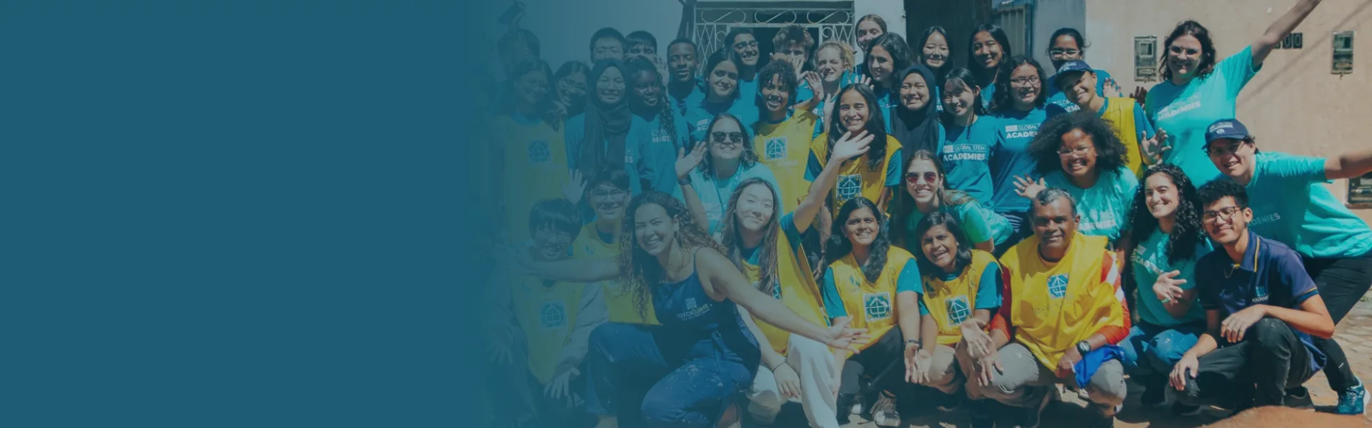 Grupo grande de voluntários da ReforAMAR e estudantes do programa Global STEM Academies, de braços abertos e sorrindo, em frente a uma casa em reforma
